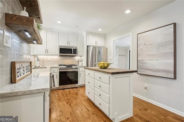 kitchen featuring light wood-type flooring, appliances with stainless steel finishes, decorative backsplash, and a kitchen island