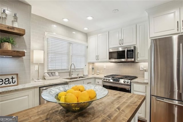 kitchen with wooden counters, sink, decorative backsplash, stainless steel appliances, and white cabinets