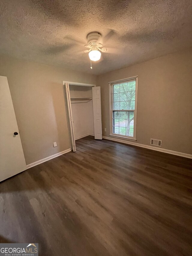 unfurnished bedroom with dark hardwood / wood-style flooring, a closet, and ceiling fan