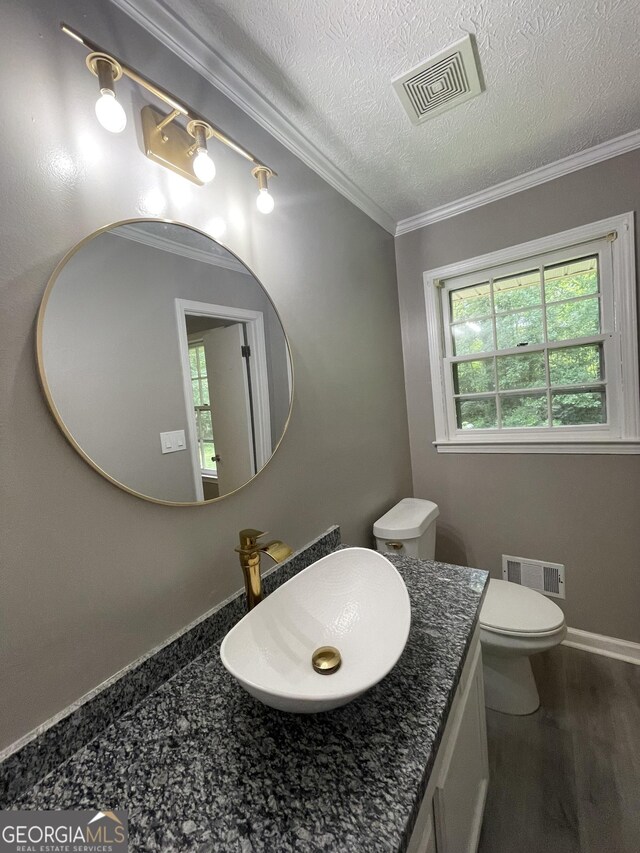 bathroom with a textured ceiling, toilet, vanity, hardwood / wood-style flooring, and ornamental molding