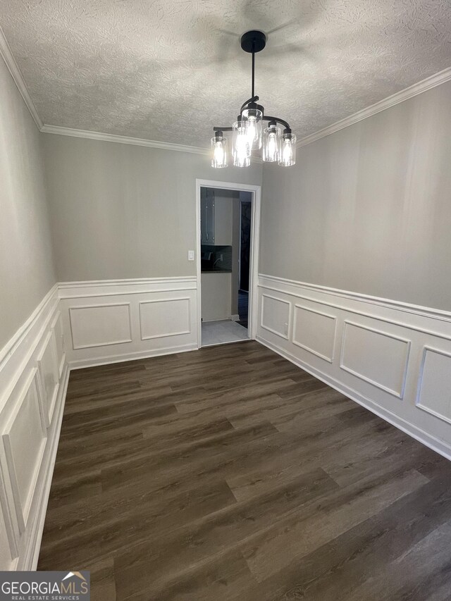 empty room with ornamental molding, an inviting chandelier, a textured ceiling, and dark wood-type flooring