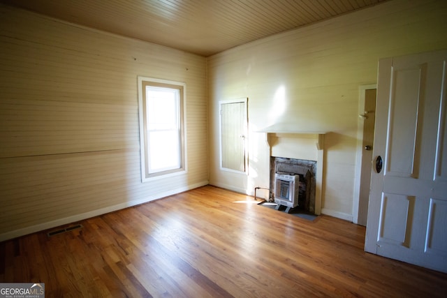 unfurnished living room with light hardwood / wood-style floors, a wood stove, wood ceiling, and wooden walls