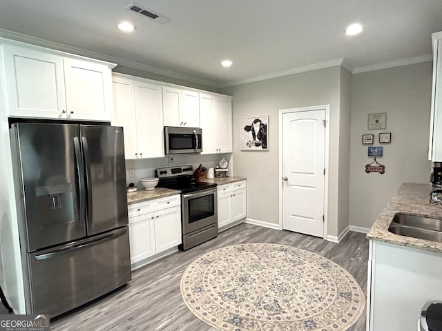 kitchen featuring wood-type flooring, white cabinets, ornamental molding, light stone countertops, and appliances with stainless steel finishes