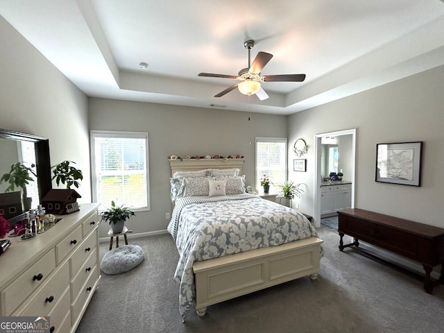 bedroom with ensuite bath, multiple windows, carpet flooring, and a tray ceiling