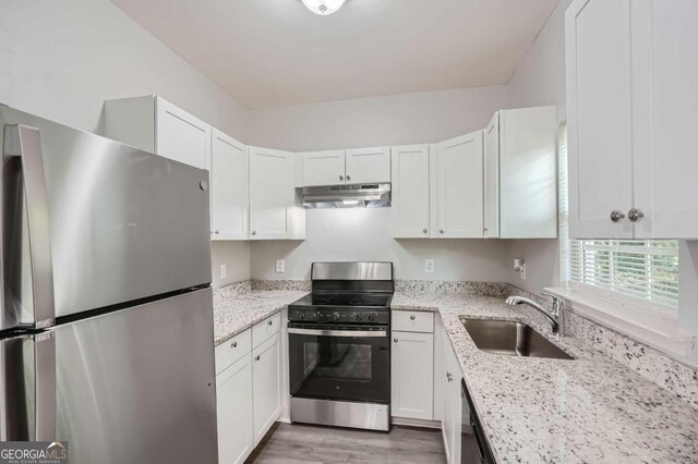 kitchen featuring appliances with stainless steel finishes, light hardwood / wood-style flooring, white cabinets, sink, and light stone countertops