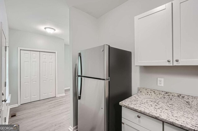 kitchen featuring white cabinetry, stainless steel fridge, light stone countertops, and light wood-type flooring