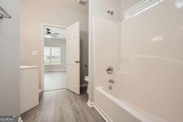 bathroom with hardwood / wood-style flooring,  shower combination, toilet, and ceiling fan