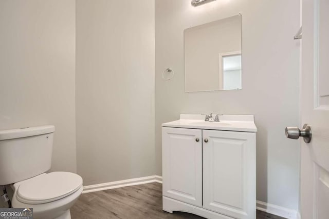 bathroom with toilet, vanity, wood finished floors, and baseboards