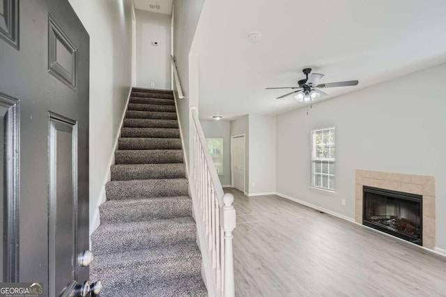 staircase with a fireplace, wood-type flooring, and ceiling fan