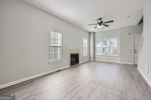 unfurnished living room with wood finished floors, ceiling fan, a tiled fireplace, baseboards, and visible vents