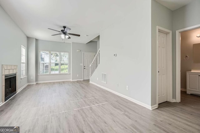 unfurnished living room with light hardwood / wood-style floors, a tiled fireplace, and ceiling fan