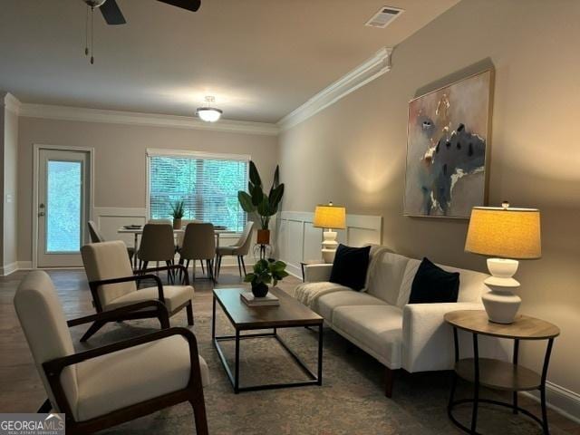 living room with ornamental molding, dark wood-type flooring, and ceiling fan