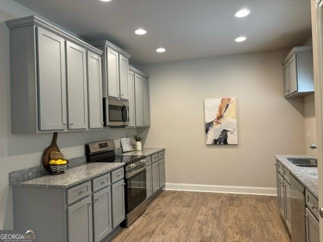 kitchen with sink, gray cabinetry, hardwood / wood-style floors, stainless steel appliances, and light stone countertops