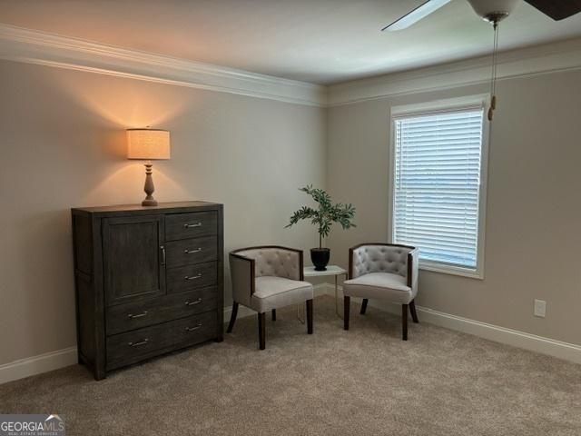 living area with ornamental molding, light colored carpet, and ceiling fan