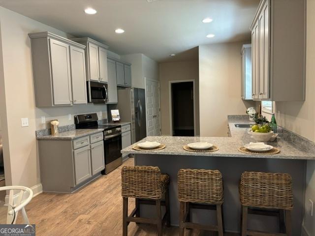 kitchen with a breakfast bar area, gray cabinetry, light hardwood / wood-style flooring, appliances with stainless steel finishes, and kitchen peninsula