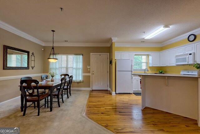 kitchen featuring light hardwood / wood-style flooring, white appliances, hanging light fixtures, crown molding, and white cabinetry