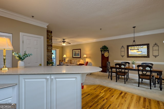 kitchen featuring decorative light fixtures, white cabinetry, light carpet, ceiling fan, and ornamental molding