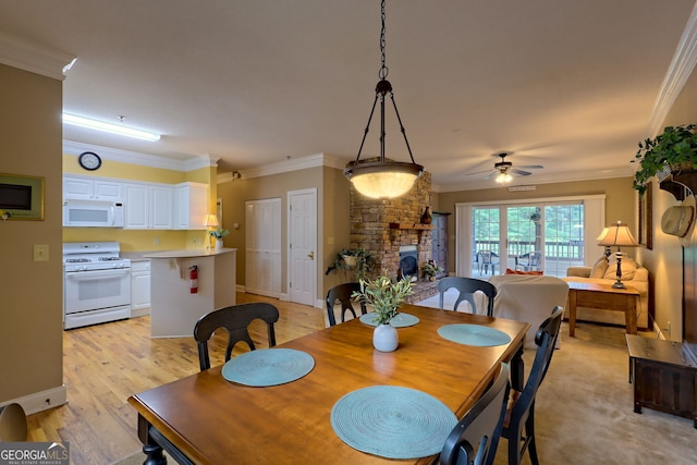 dining space with a stone fireplace, light hardwood / wood-style floors, crown molding, and ceiling fan