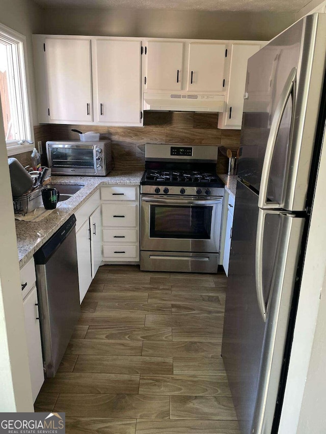 kitchen featuring white cabinetry, dark hardwood / wood-style floors, light stone countertops, appliances with stainless steel finishes, and sink