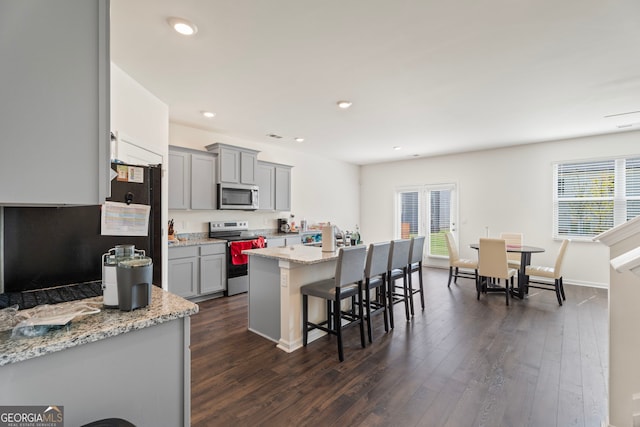 kitchen with a kitchen bar, gray cabinetry, a center island, appliances with stainless steel finishes, and light stone countertops