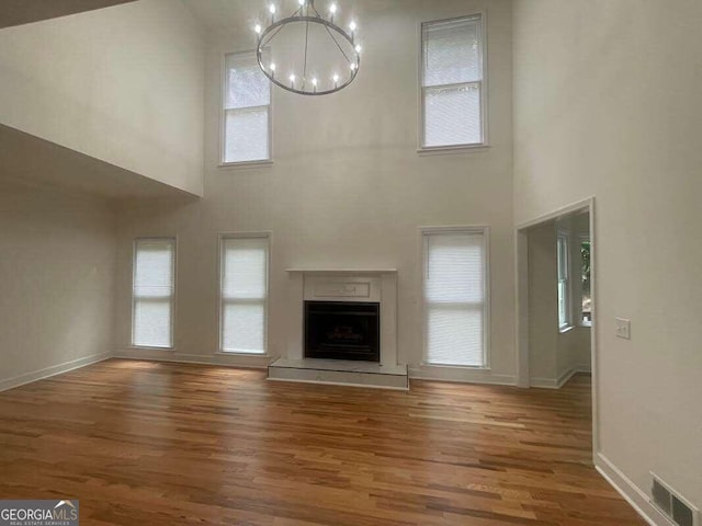 unfurnished living room featuring a high ceiling, hardwood / wood-style flooring, a wealth of natural light, and an inviting chandelier