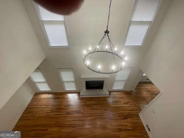 unfurnished living room with a high ceiling, hardwood / wood-style floors, a wealth of natural light, and an inviting chandelier