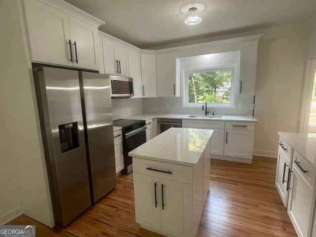 kitchen with wood finished floors, a sink, light countertops, appliances with stainless steel finishes, and backsplash