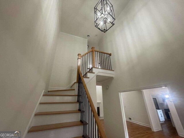 staircase with wood-type flooring, a notable chandelier, and a towering ceiling