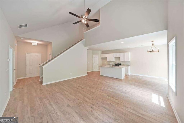 unfurnished living room with light wood-type flooring, ceiling fan with notable chandelier, and high vaulted ceiling