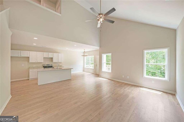 unfurnished living room featuring high vaulted ceiling, sink, ceiling fan with notable chandelier, and light hardwood / wood-style floors