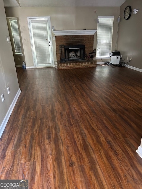 unfurnished living room featuring dark hardwood / wood-style floors and a brick fireplace