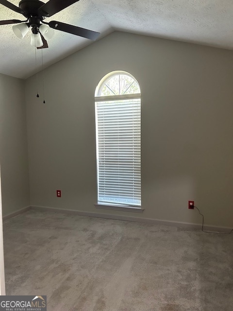 empty room with ceiling fan, vaulted ceiling, and a textured ceiling