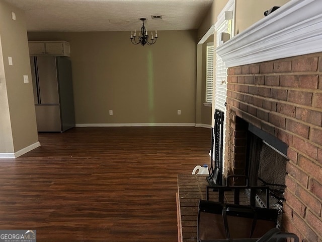 unfurnished living room featuring dark wood-type flooring, a notable chandelier, a textured ceiling, and a brick fireplace