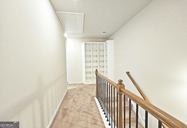 hallway with visible vents, attic access, light carpet, an upstairs landing, and baseboards