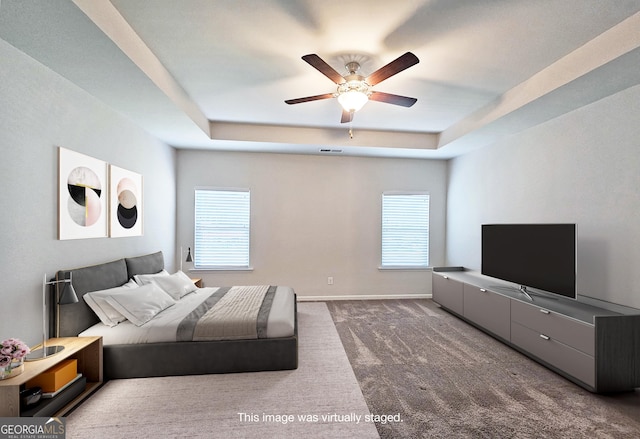 carpeted bedroom with a tray ceiling, multiple windows, and baseboards