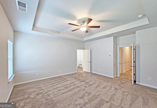 unfurnished bedroom with carpet floors, a tray ceiling, visible vents, and baseboards