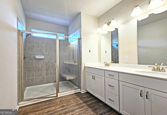 full bath with double vanity, a sink, a shower stall, and wood finished floors