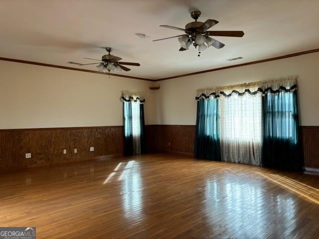 empty room featuring hardwood / wood-style floors, ceiling fan, wooden walls, and ornamental molding