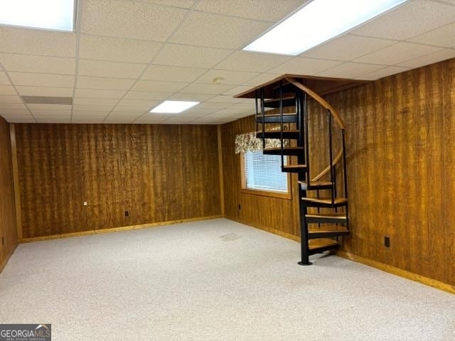 basement with light colored carpet, wooden walls, and a drop ceiling