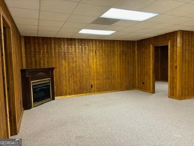 unfurnished living room featuring carpet, wooden walls, and a drop ceiling