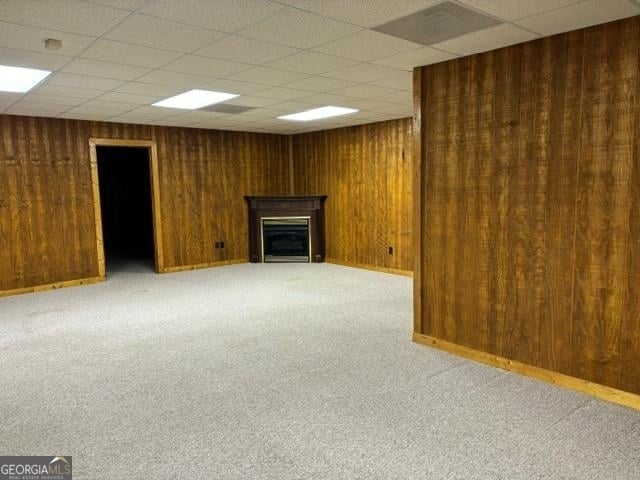 basement with wood walls, light colored carpet, and a paneled ceiling