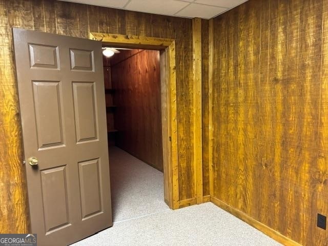 corridor featuring carpet, wooden walls, and a drop ceiling