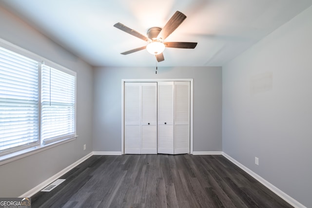 unfurnished bedroom with multiple windows, dark hardwood / wood-style flooring, a closet, and ceiling fan