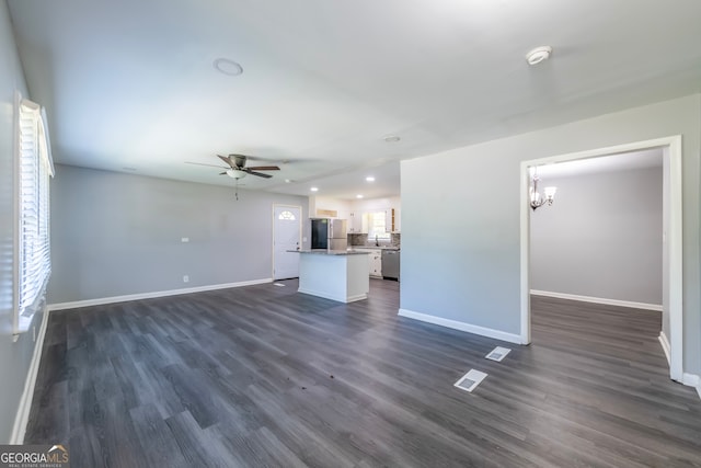 unfurnished living room with plenty of natural light, ceiling fan with notable chandelier, and dark hardwood / wood-style flooring