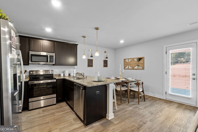 kitchen with light stone countertops, kitchen peninsula, decorative light fixtures, appliances with stainless steel finishes, and light wood-type flooring