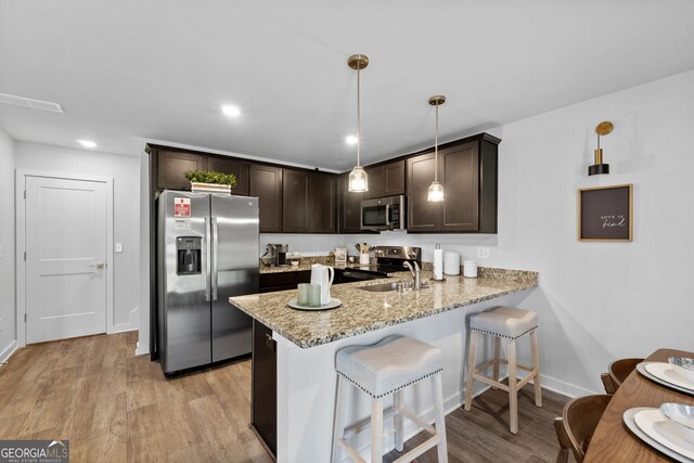 kitchen with light hardwood / wood-style floors, kitchen peninsula, stainless steel appliances, decorative light fixtures, and dark brown cabinetry