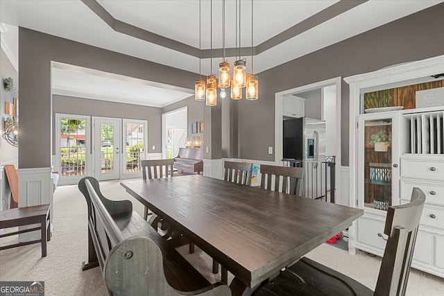 carpeted dining space with an inviting chandelier, french doors, and a tray ceiling