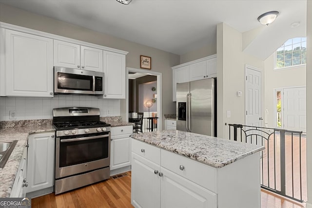 kitchen featuring white cabinetry, stainless steel appliances, backsplash, and light wood-type flooring