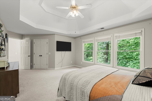 bedroom featuring ceiling fan, light carpet, and a tray ceiling