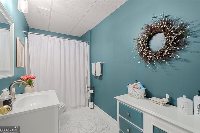 bathroom with tile patterned flooring, a drop ceiling, toilet, and vanity